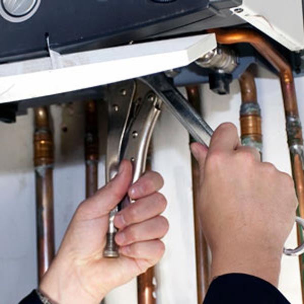 Close-up of a technician using a wrench on plumbing pipes, a service provided by Mann Plumbing & Heating.