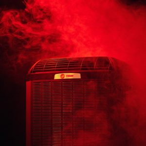 Trane HVAC unit surrounded by dramatic red smoke, installed and serviced by Mann Plumbing & Heating.